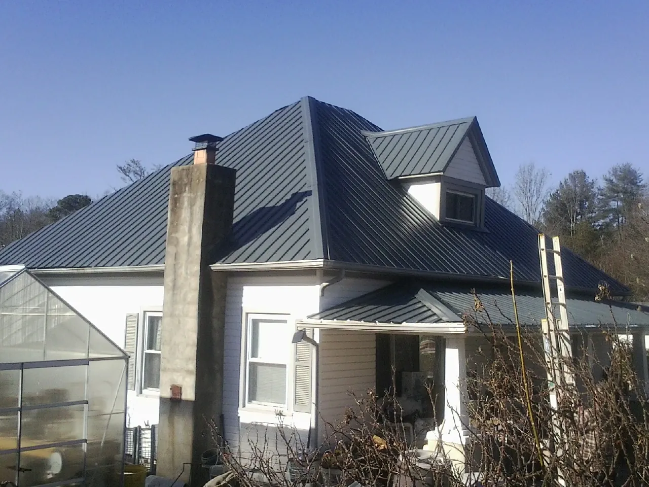 Dark blue standing seam metal roof on a white farmhouse with dormer — Slate & Tile Roof Repair by Roofing Brothers in Lake Lynn