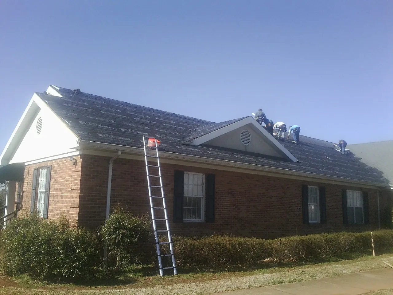 Crew tearing shingles off a brick ranch roof with a ladder set — Metal Roof Repair work by our crew in Lake Lynn