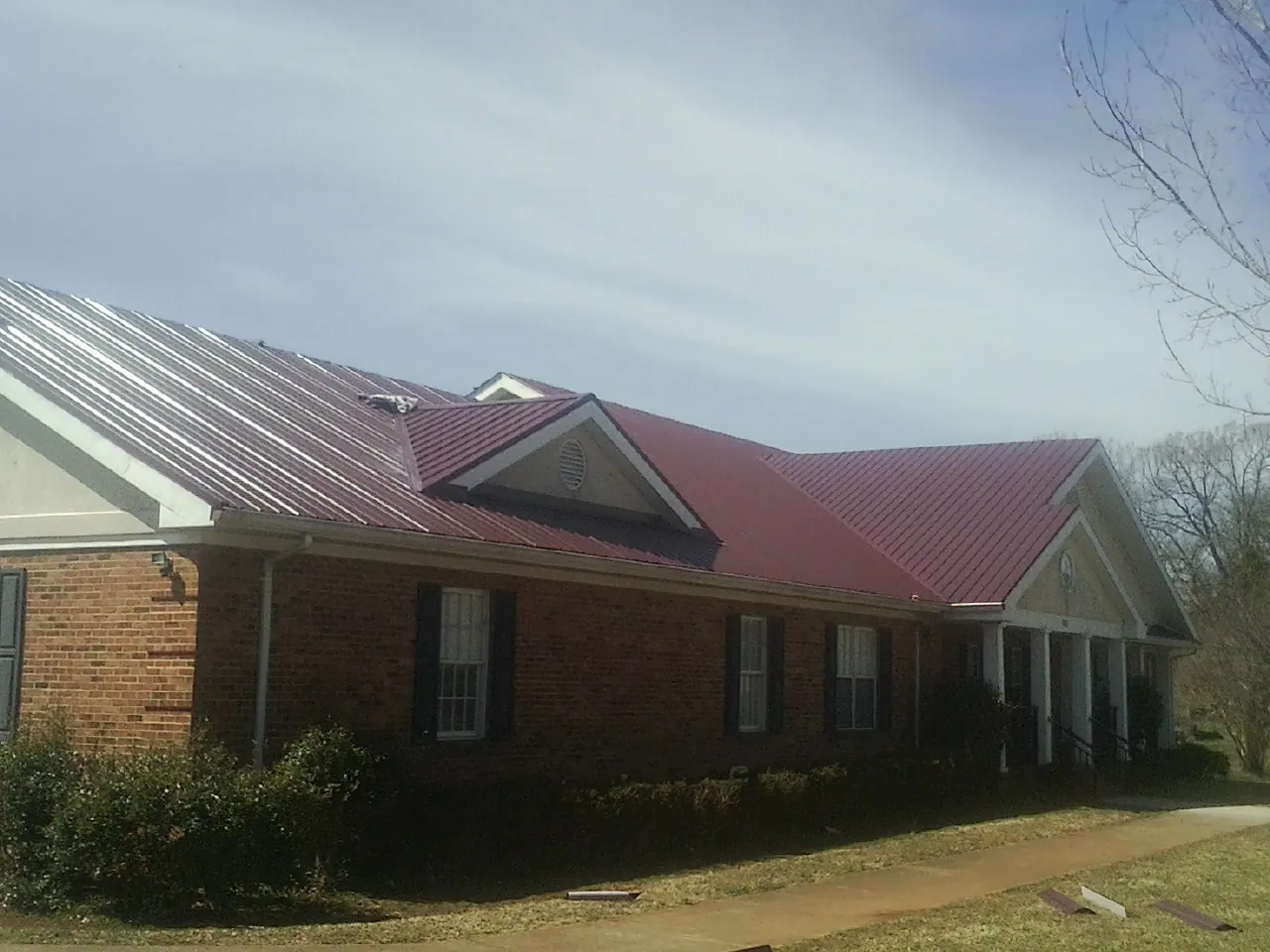 Red metal roof with gabled entries on a long brick building, from a Hail Damage Roof Repair job in Lake Lynn