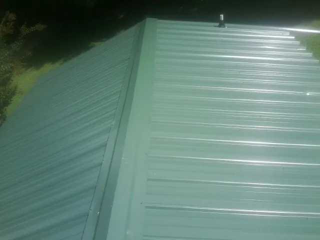 New green metal panels meeting at the ridge of a roof — Flat Roof Repair work by our crew in Lake Lynn
