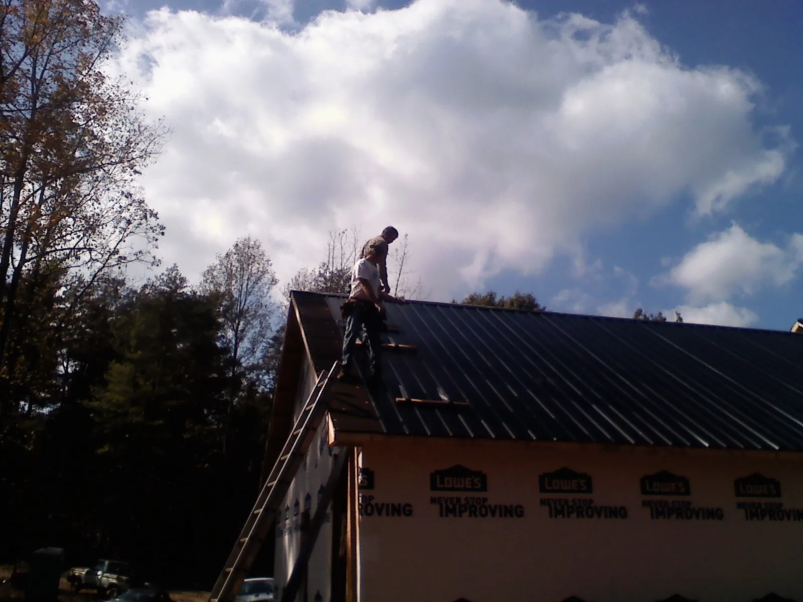 Roofer fastening dark metal panels high against a cloudy sky, from a Roof Inspection job in Lake Lynn
