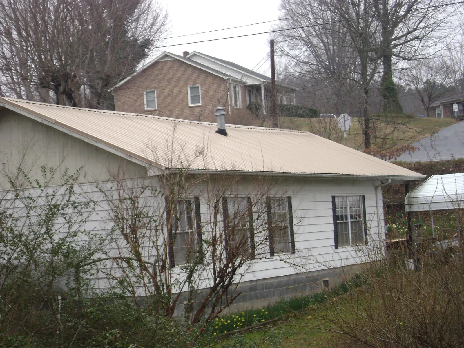 Tan metal roof on a white sided house set into a hillside — Commercial Roofing by Roofing Brothers in Lake Lynn