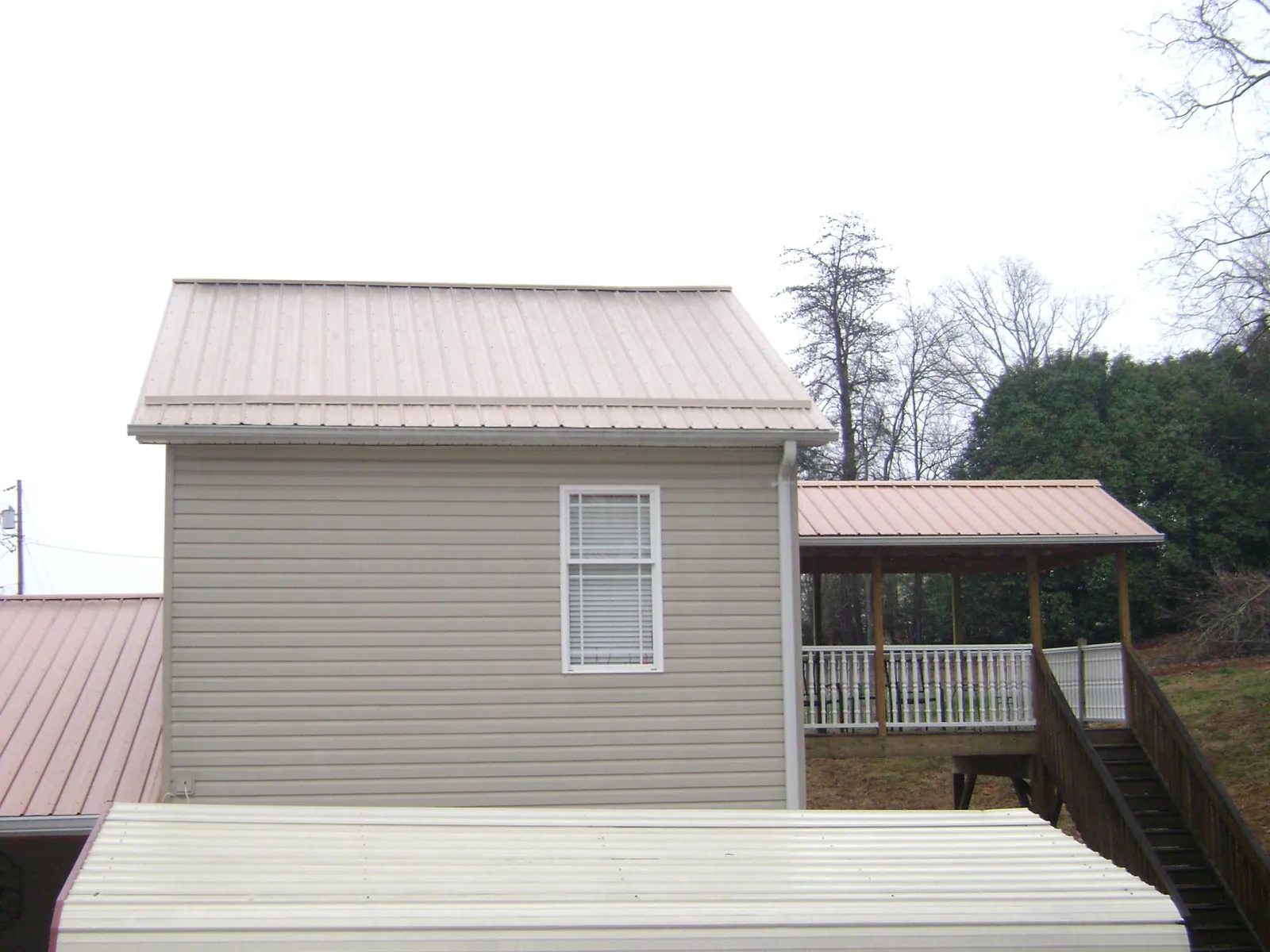 Tan metal roofs on a two story addition and attached porch, from a Roof Replacement job in Lake Lynn